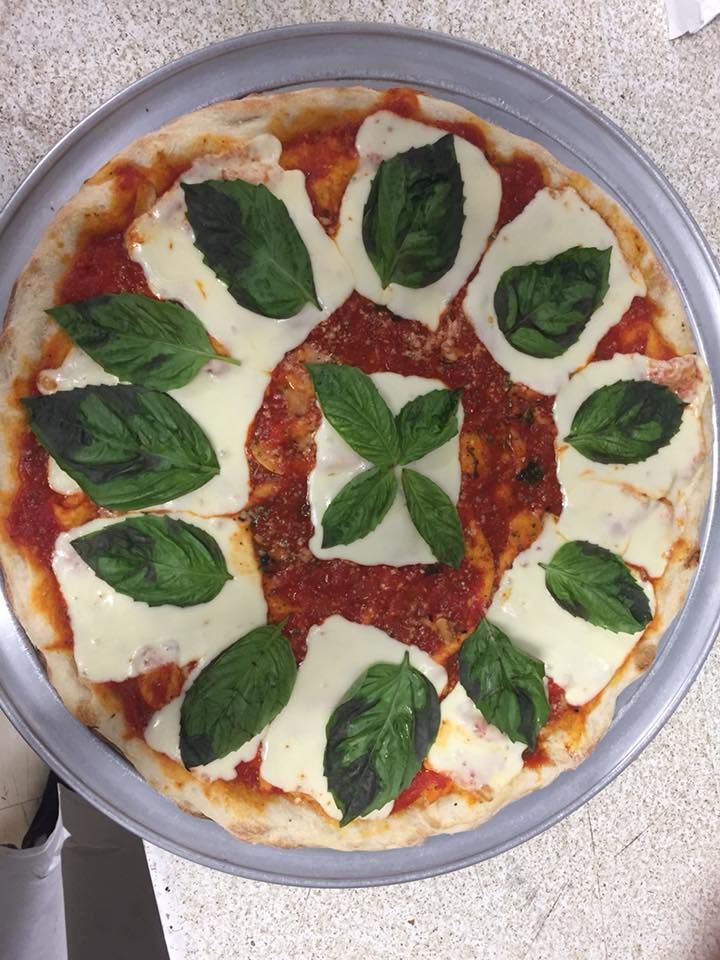 Pizza with tomato sauce, mozzarella, and basil leaves arranged in a circular pattern on a metal tray.