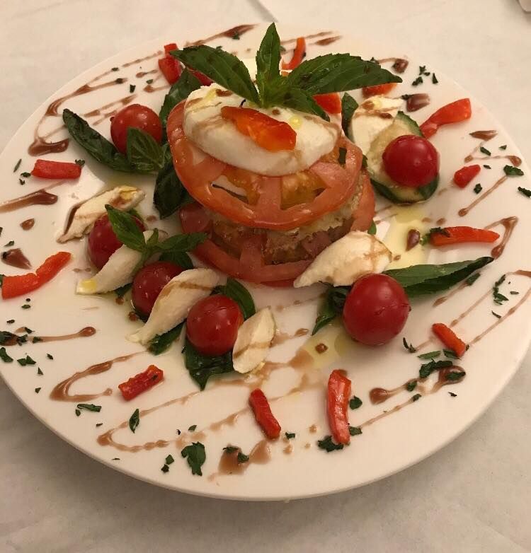 Caprese salad with tomato, mozzarella, basil, and balsamic glaze on a white plate.