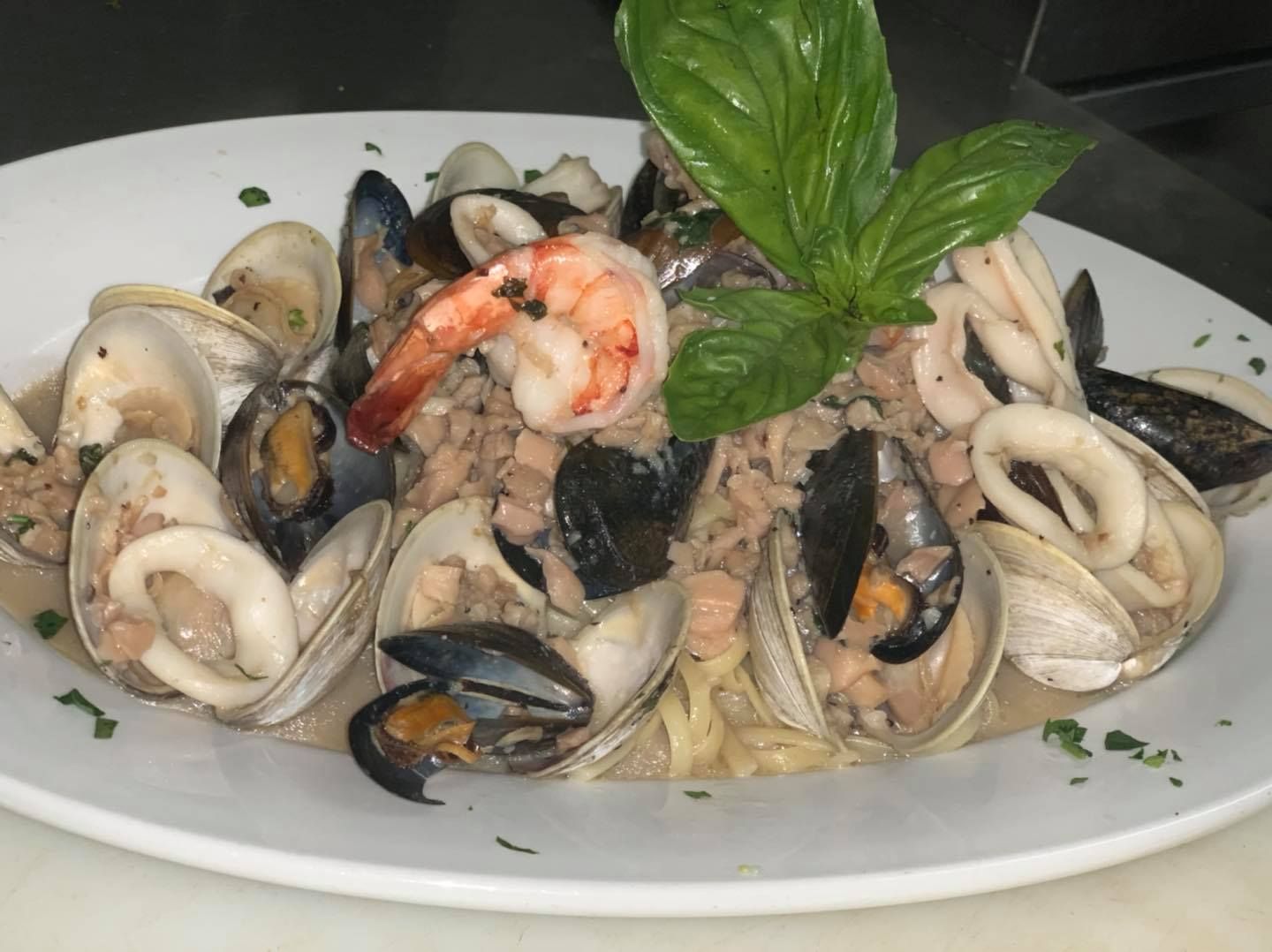 Seafood pasta with clams, mussels, shrimp, and basil garnish on a white plate.