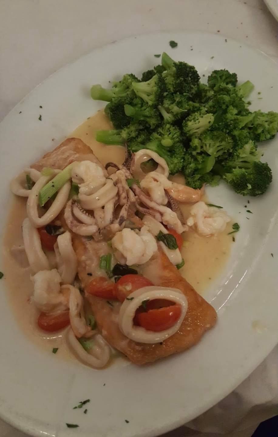 Plate of fish, squid, and tomatoes in sauce, with a side of broccoli.