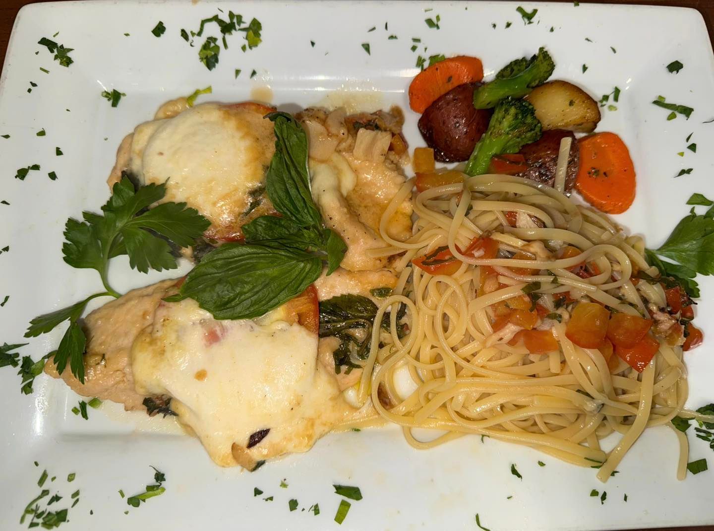 Chicken, pasta, and roasted vegetables on a white plate, garnished with parsley.