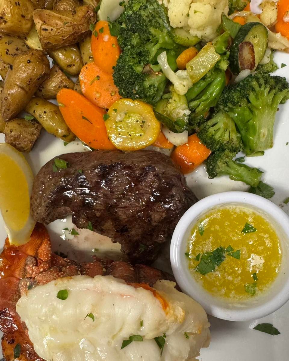 Plate with steak, lobster tail, roasted vegetables, potatoes, and butter sauce.