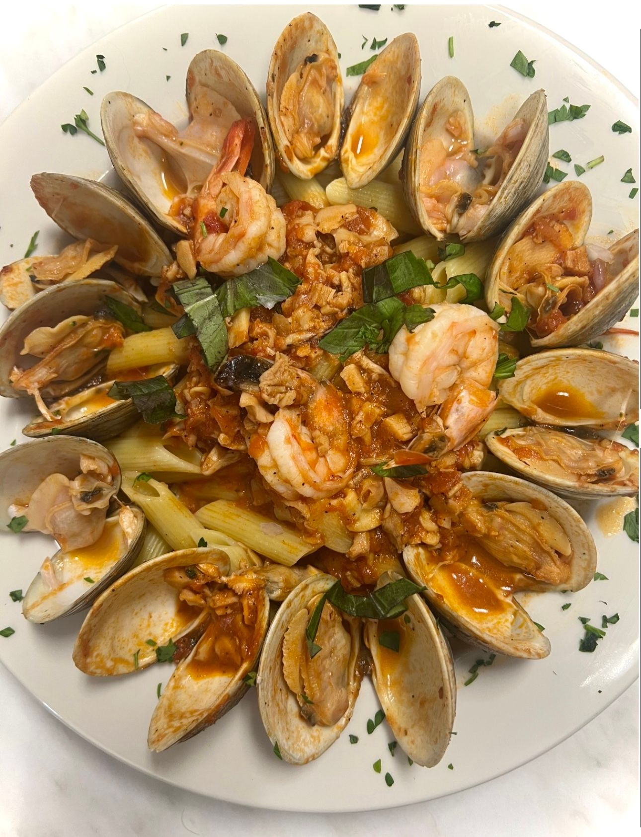 Pasta dish with clams, shrimp, and tomato sauce, arranged on a white plate, garnished with herbs.