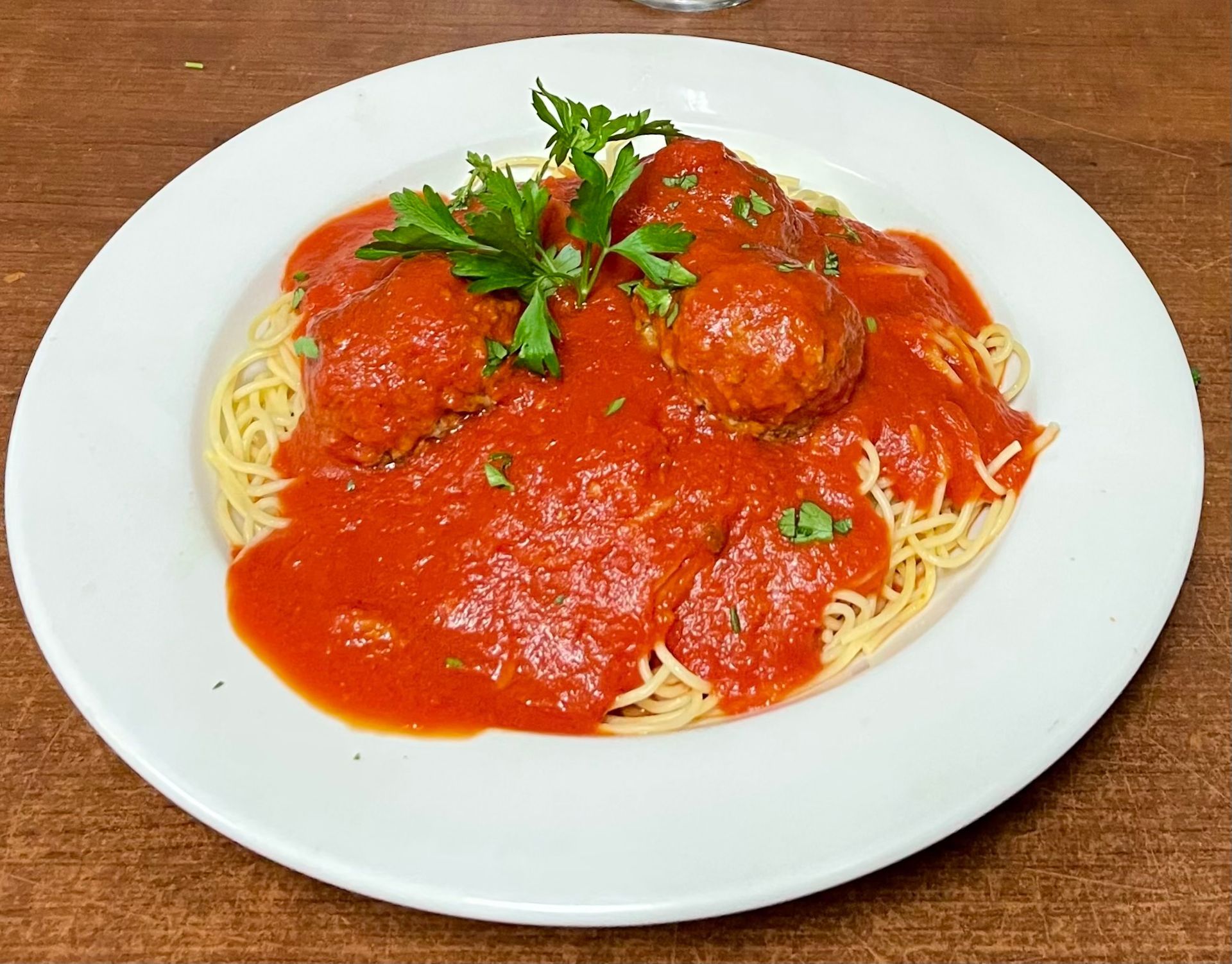 Spaghetti and meatballs in red sauce, garnished with parsley, on a white plate.