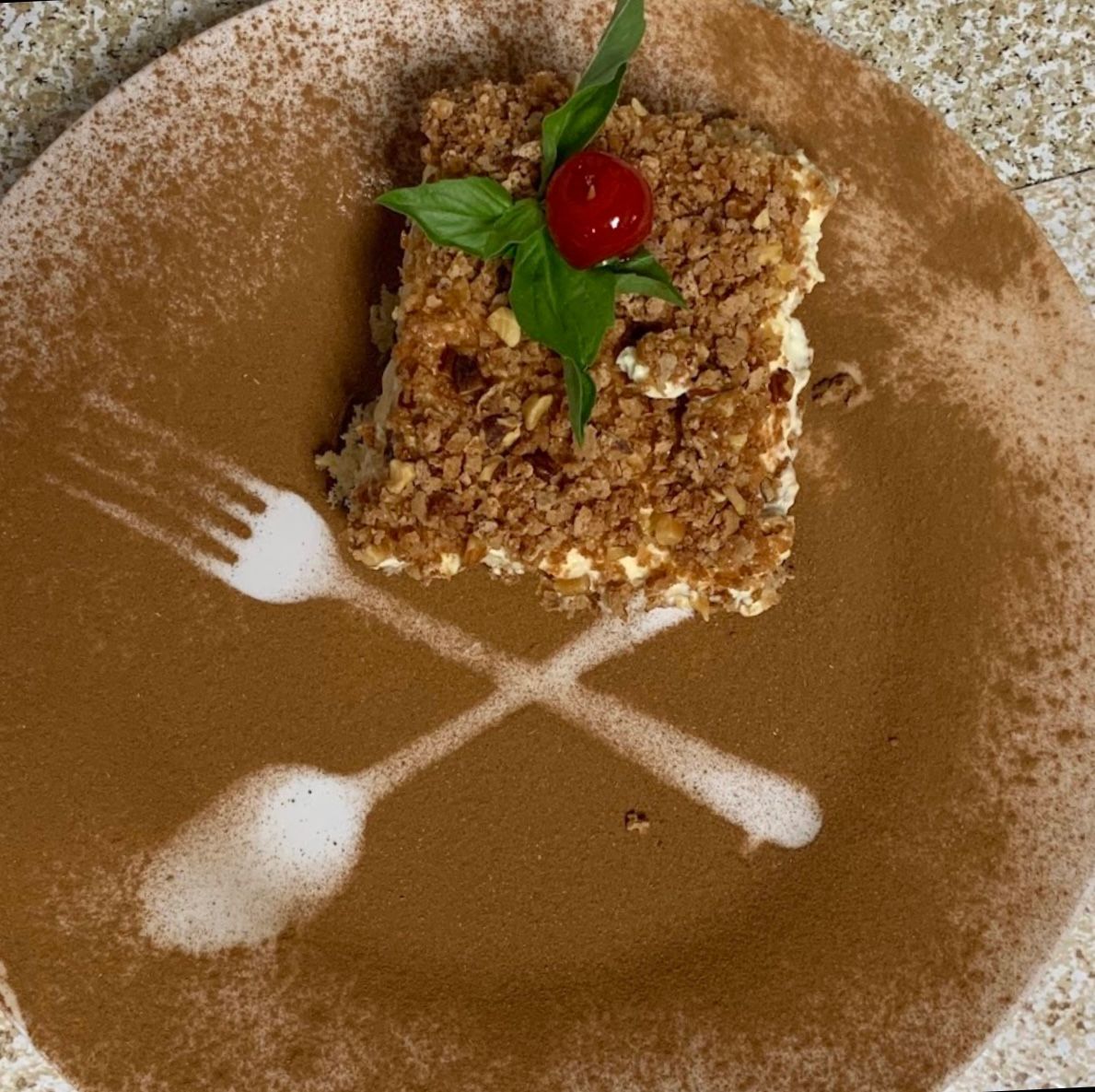 Slice of dessert on plate decorated with cocoa and a fork silhouette.