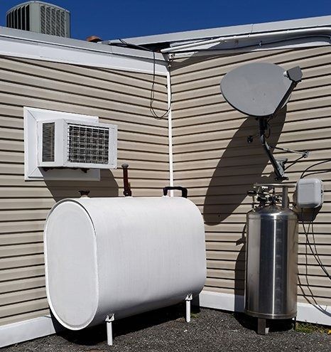 Backyard propane tank, satellite dish, and window AC unit beside a house.
