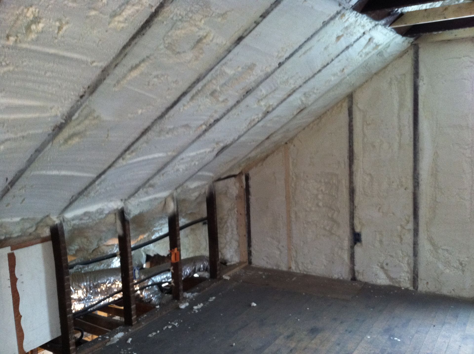 Attic space insulated with light-colored spray foam between rafters and wall studs.
