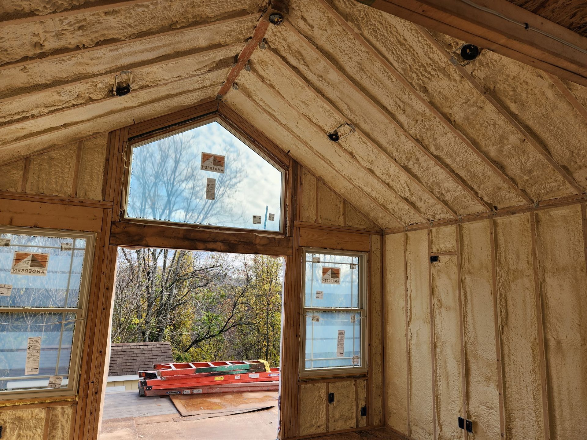 Interior of a building under construction, covered in spray foam insulation. Windows and door frames are visible.