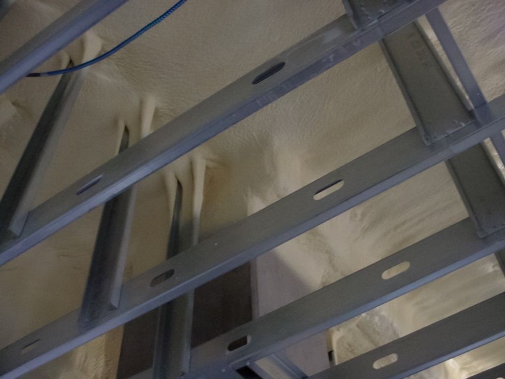 Metal framing with spray foam insulation in a ceiling, viewed from below.