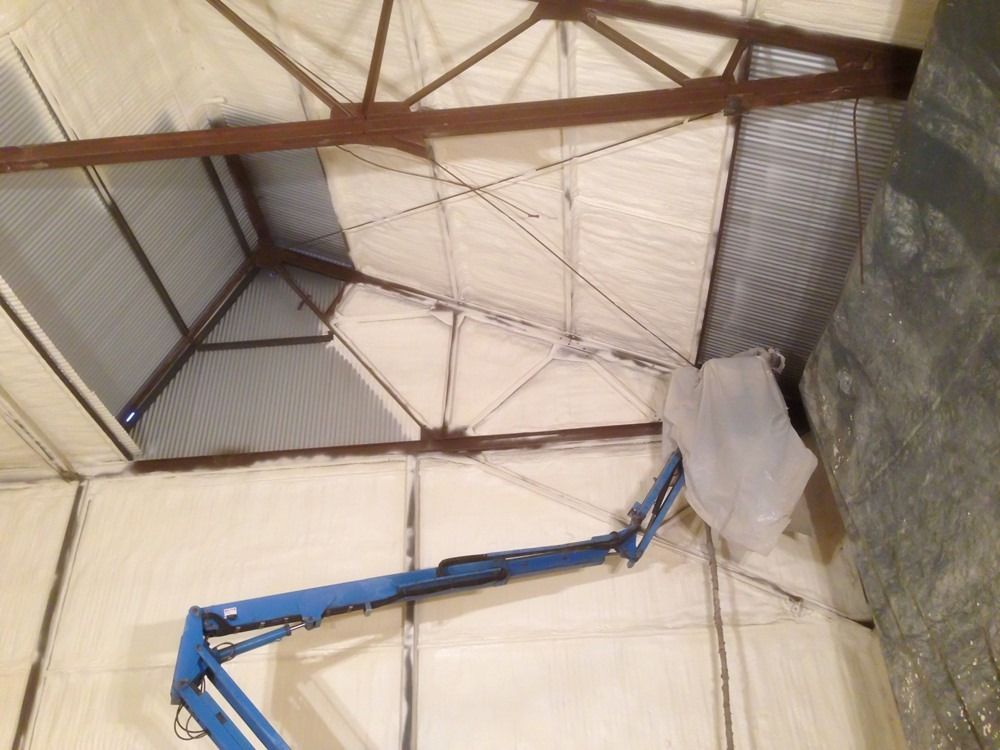 Blue lift spraying insulation on interior walls and ceiling of a building.