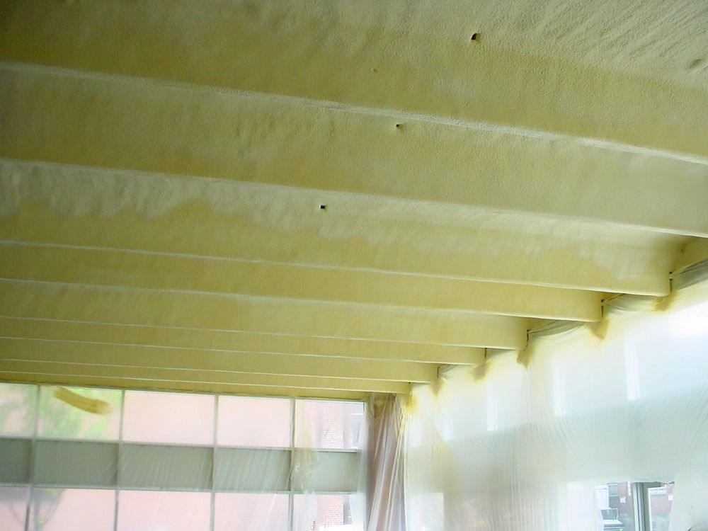 Yellow spray foam insulation covering wooden beams in a building.