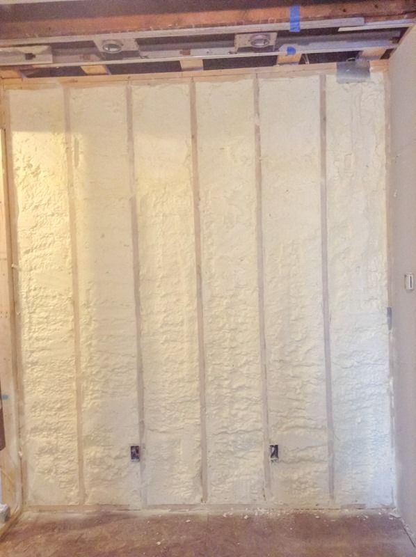 Foam insulation sprayed on a wall between wooden studs. Beige foam fills the spaces.