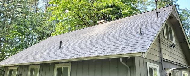 Gray shingled house roof with black vents, surrounded by green trees