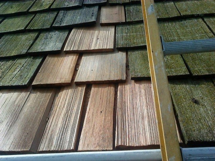 Damaged cedar shingle roof with missing and mismatched shingles beside a vertical metal flashing strip