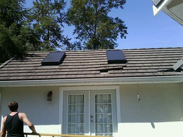 Person on a patio facing a white house roof with two black solar panels under a blue sky