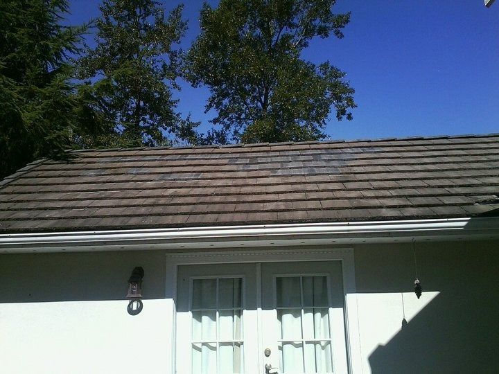 White house exterior with brown shingled roof, double doors, and trees against a blue sky