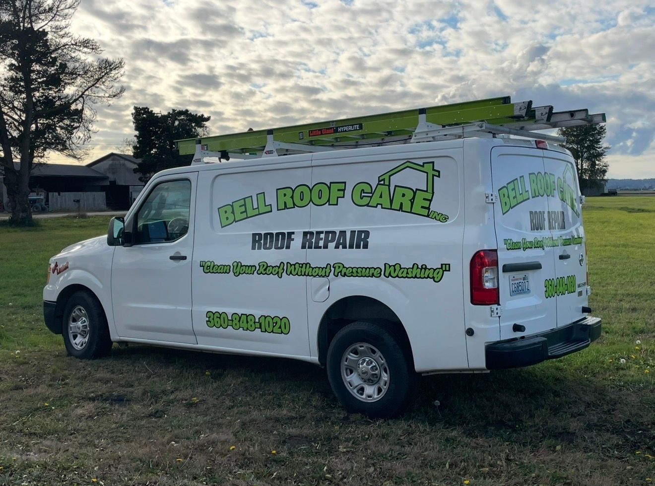 White roofing service van with green lettering parked on grass beside a house