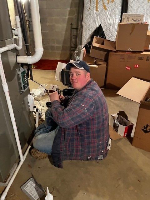 A man is kneeling down in a basement working on a heater.
