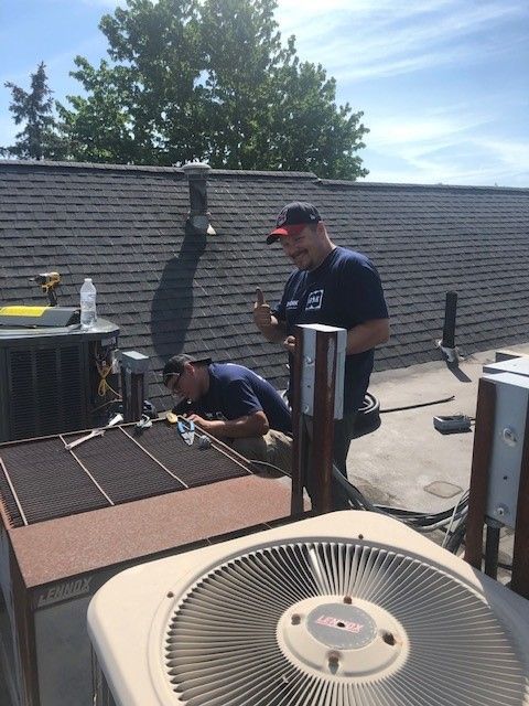 Two men are working on an air conditioner on a roof