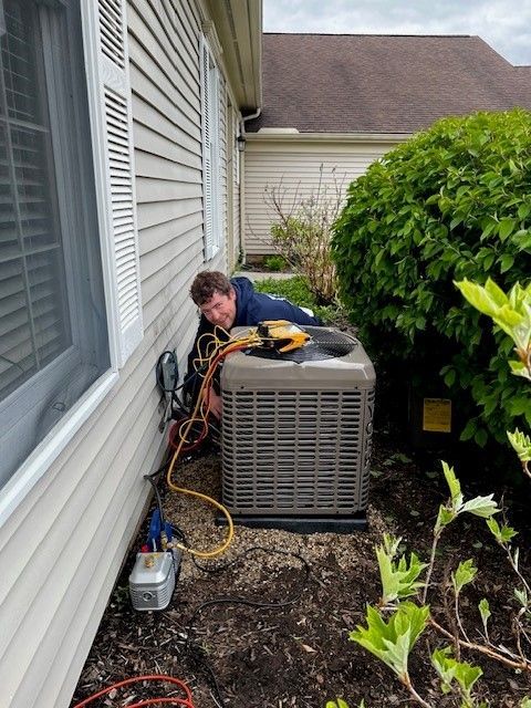 A man is working on an air conditioner outside of a house.