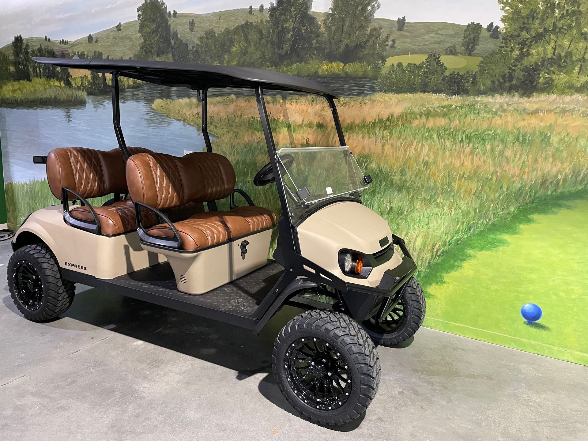 Beige golf cart with black accents parked near a painted golf course scene.