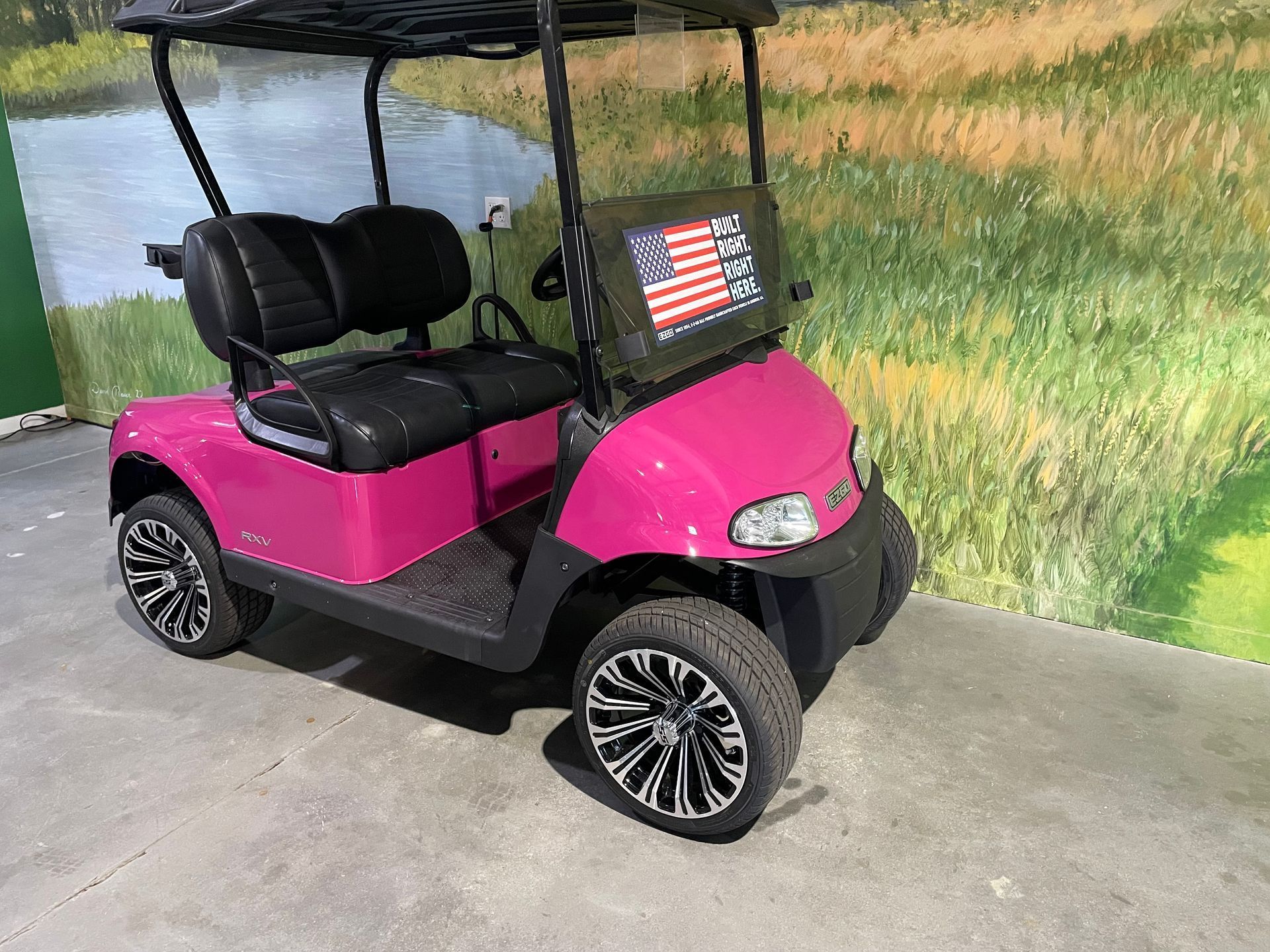 Pink golf cart with black seats, black wheels, and a patriotic American flag on the front.