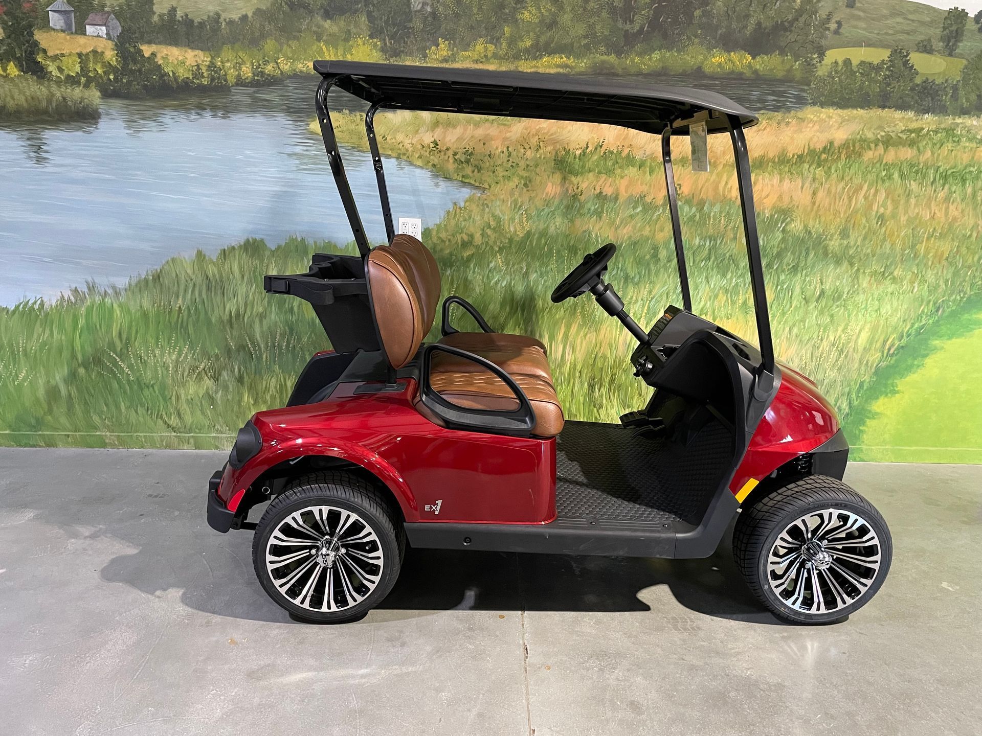Red golf cart parked on a concrete surface, with a lake and grass backdrop.