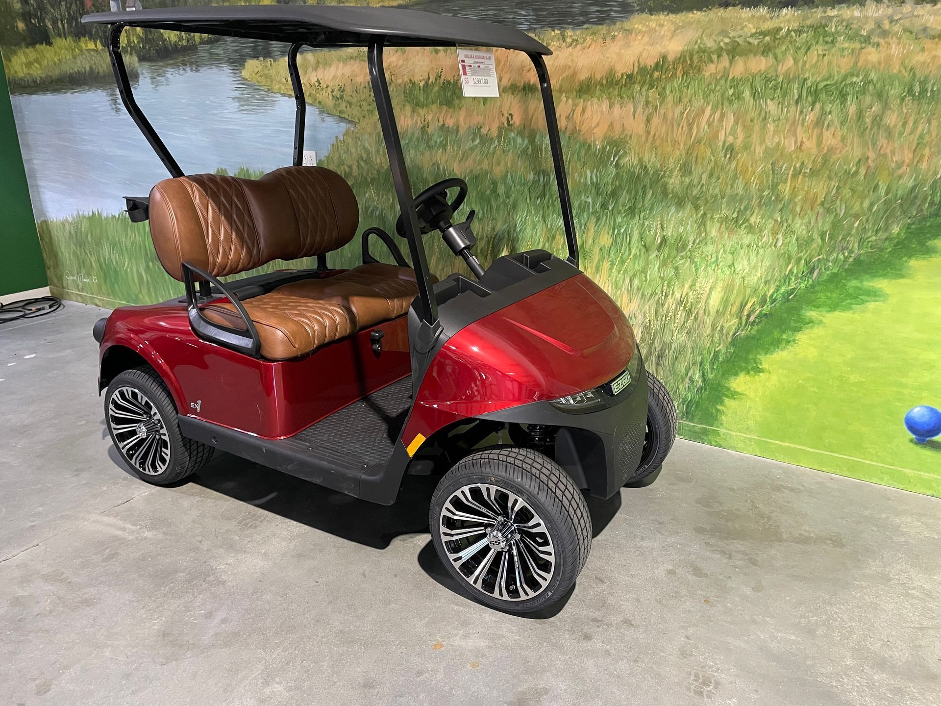 Red golf cart with brown seats, black roof, and decorative wheels on a concrete surface.