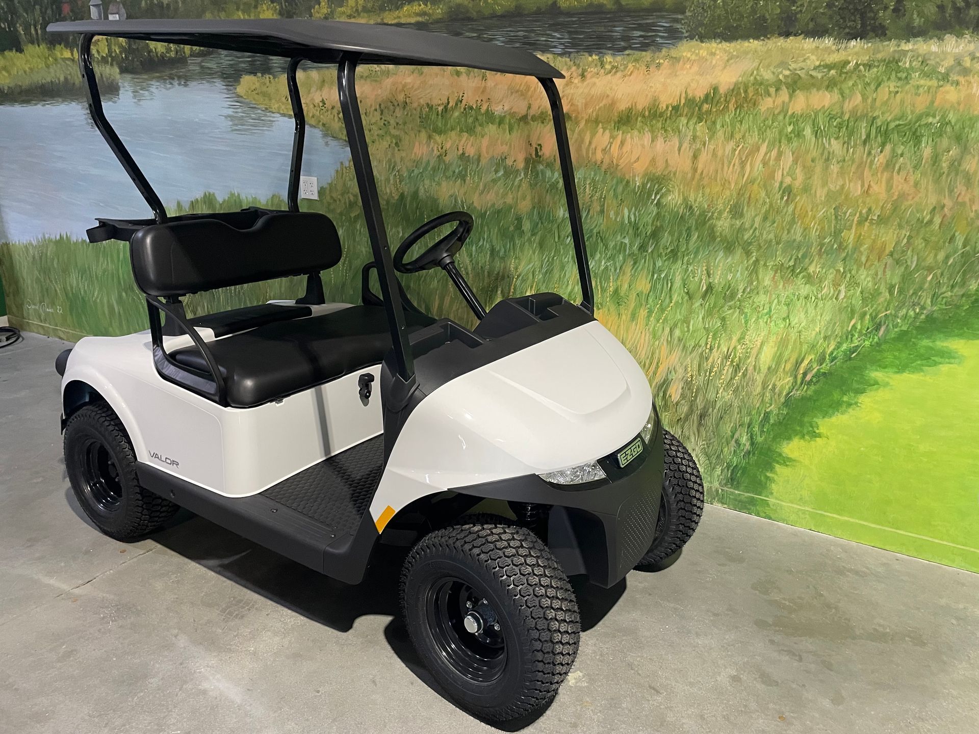 White golf cart with black accents and off-road tires, parked in front of a golf course scene.