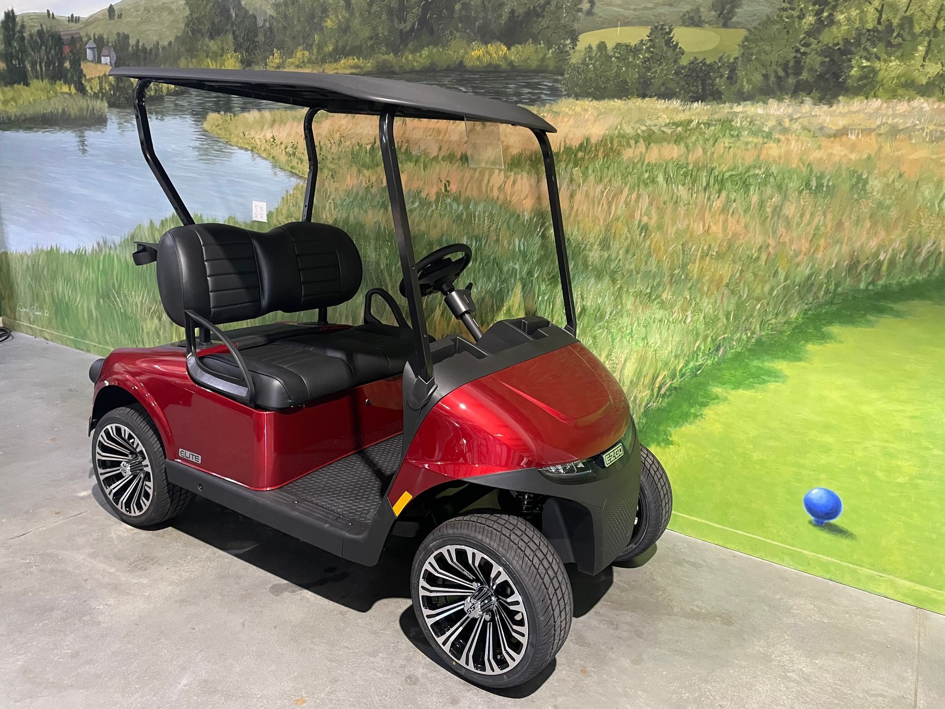 Red golf cart with black roof and seating on display at a golf course.