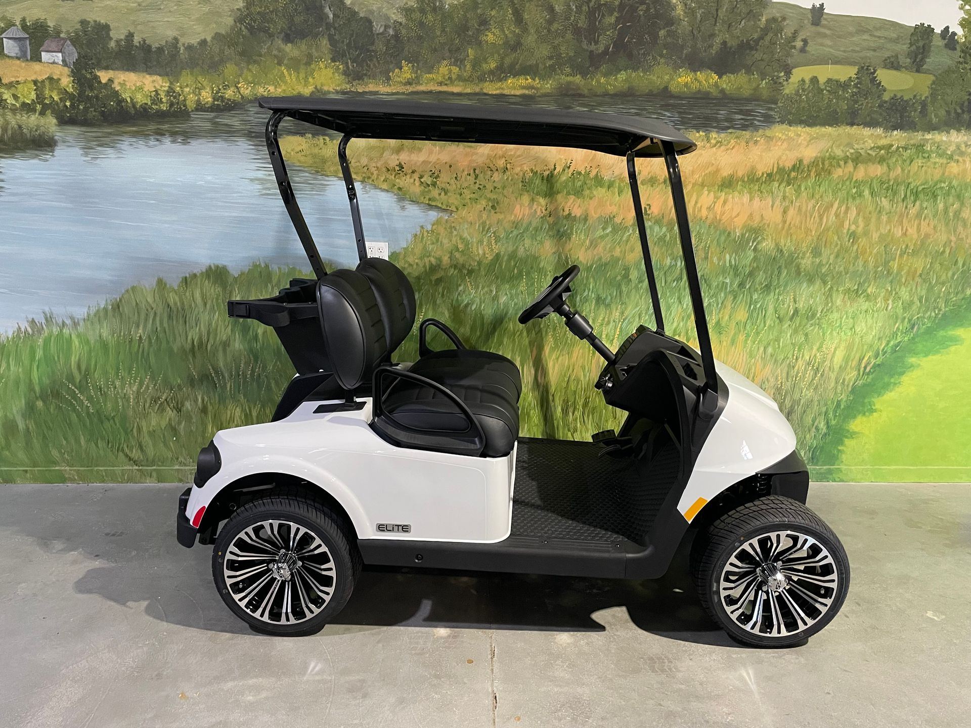 White golf cart with black accents, parked in front of a painted golf course scene.