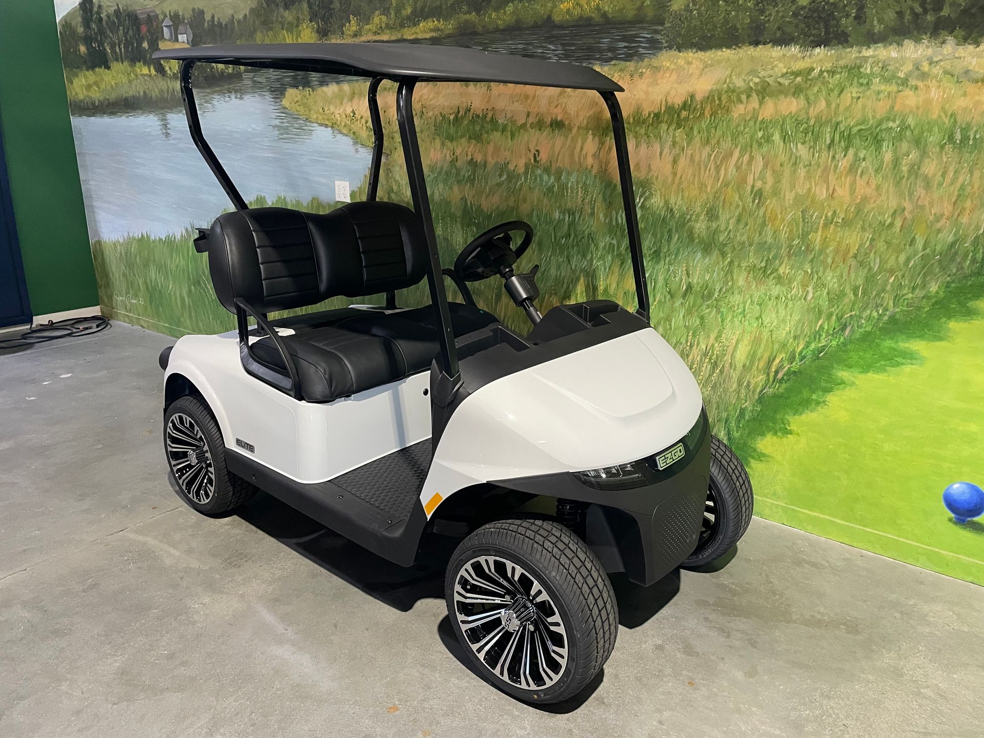 White and black golf cart on a pathway with a green and blue background.