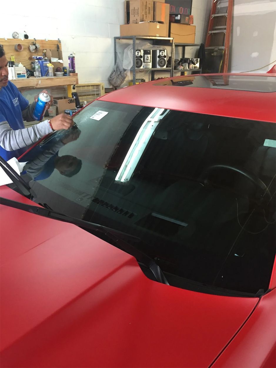 A man is cleaning the windshield of a red car
