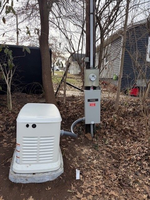 Outdoor electrical and HVAC equipment beside a house in a wooded yard