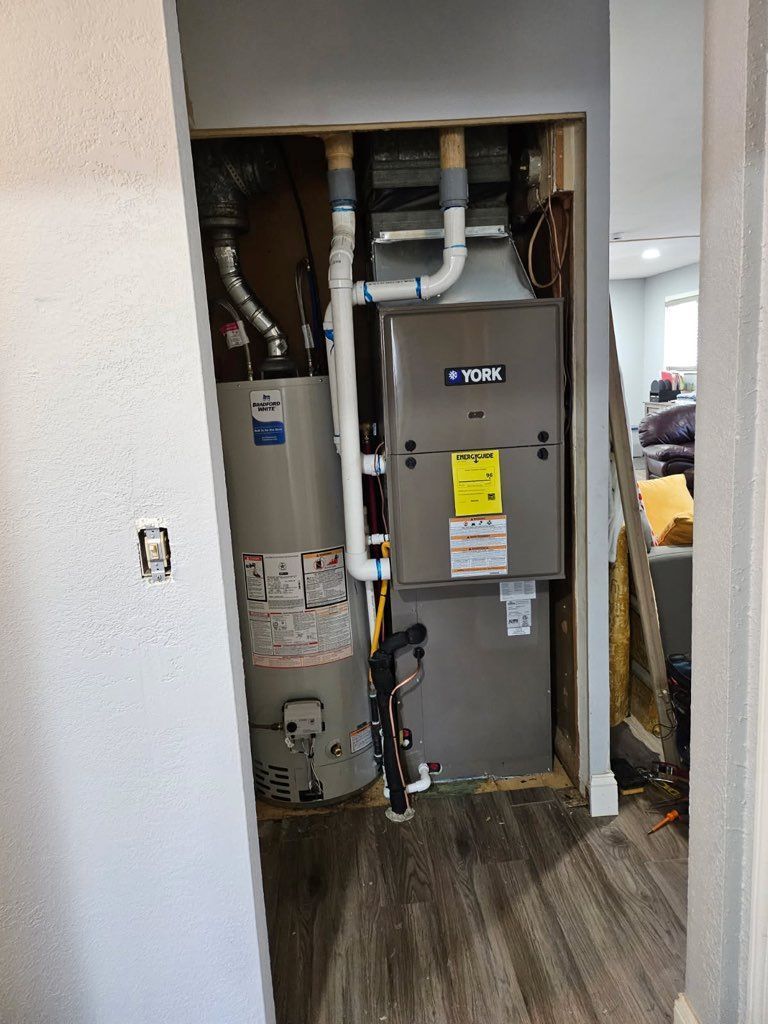 Open utility closet with furnace, water heater, and exposed plumbing in a hallway.