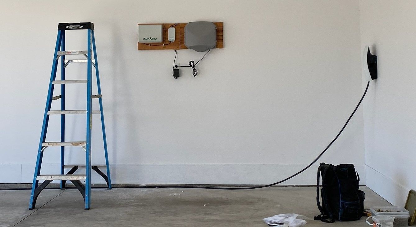 Blue ladder in a bare room beside a wall-mounted shelf, with a cable running to a black bag on the floor.