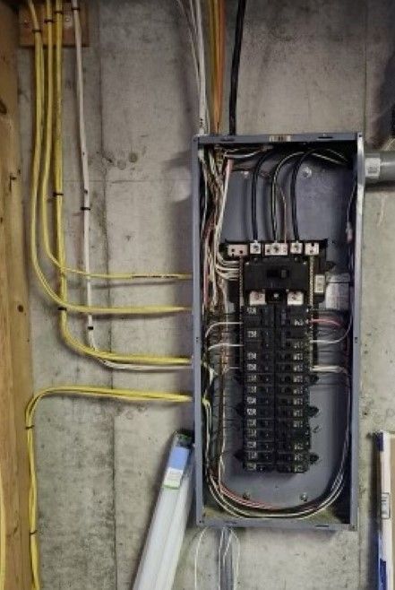 Open electrical breaker panel with exposed wiring in a concrete utility room