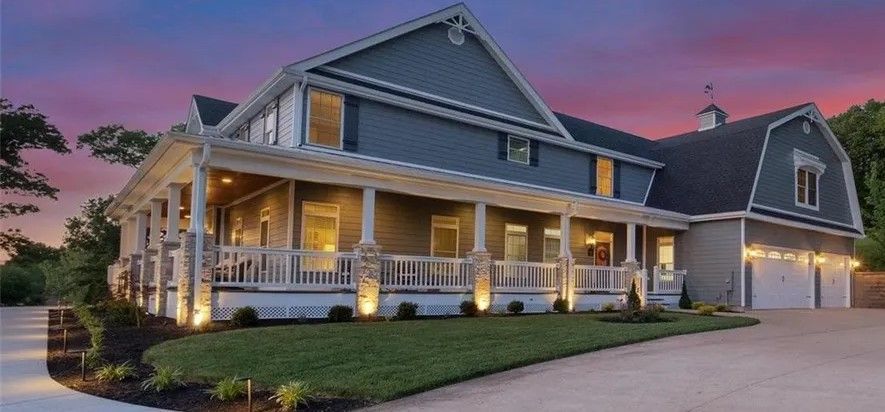 Large gray house with lit front porch and garage at dusk