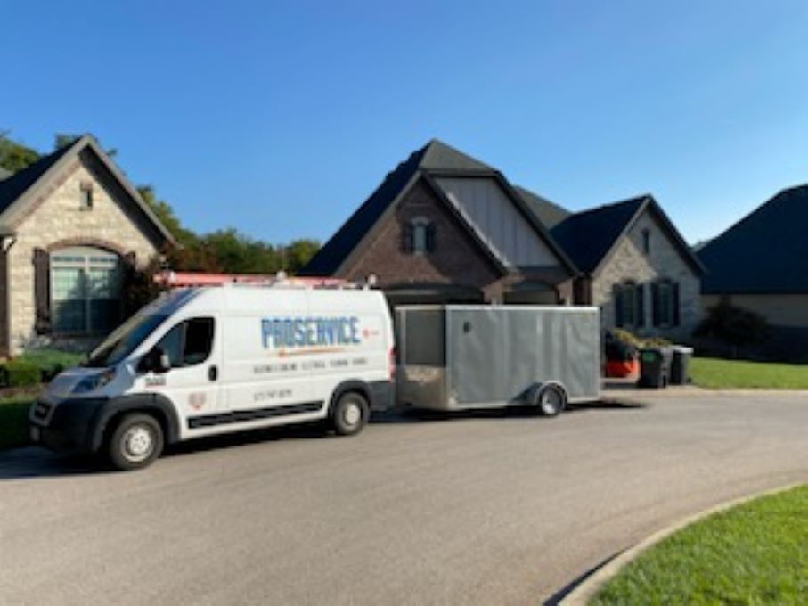 White service van with a trailer parked on a suburban street in front of brick houses.