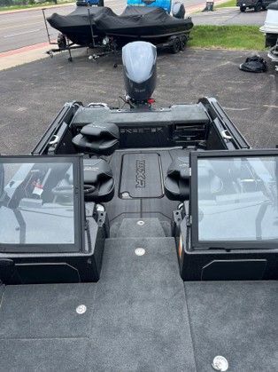 Fishing boat helm with twin electronic displays on a carpeted deck, docked near the water