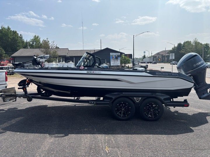 White and black motorboat on trailer in a parking lot, with an outboard engine and marina in the background