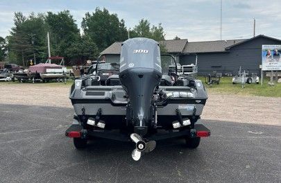 Rear view of a gray bass boat with a Mercury outboard on a trailer in a parking lot.