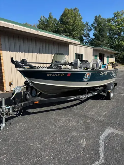 Blue fishing boat on a trailer parked beside a tan building in a sunlit lot