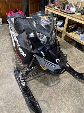 Black Ski-Doo snowmobile with orange accents parked inside.