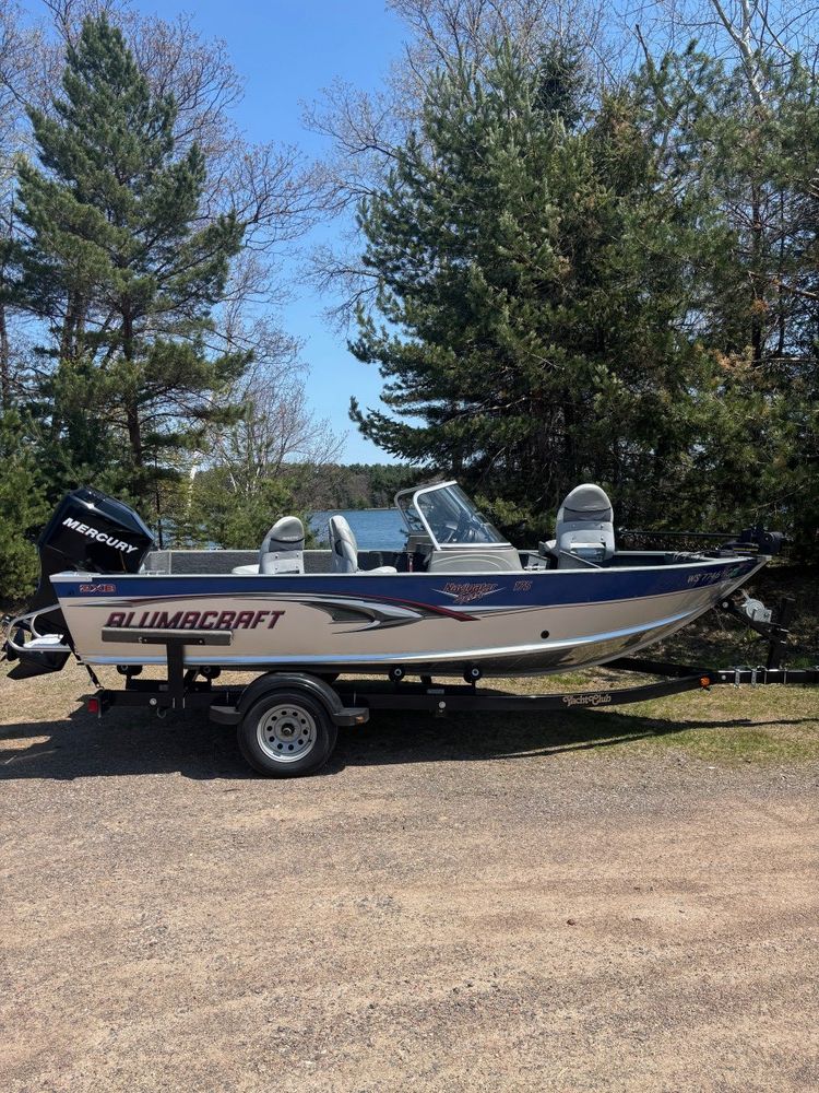A fishing boat is parked in a parking lot next to trees.