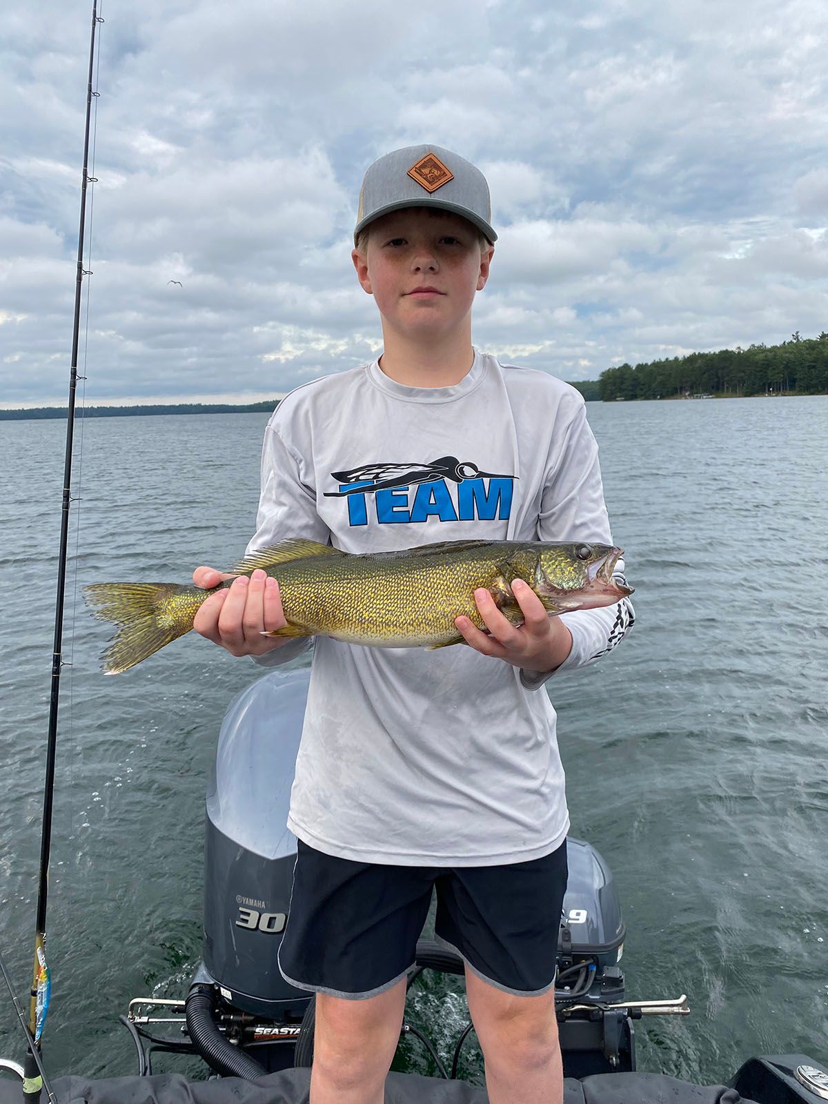 A young boy is standing on a boat holding a walleye fish