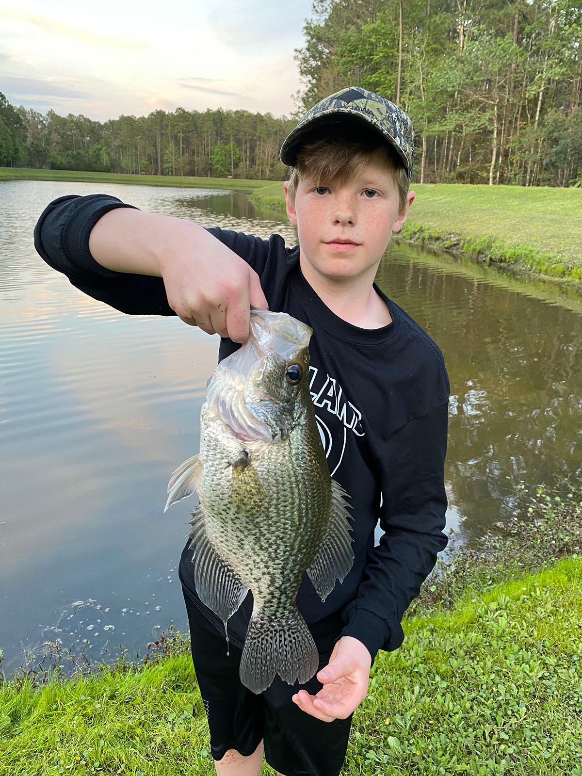 A young boy is holding a fish in his hands in front of a lake