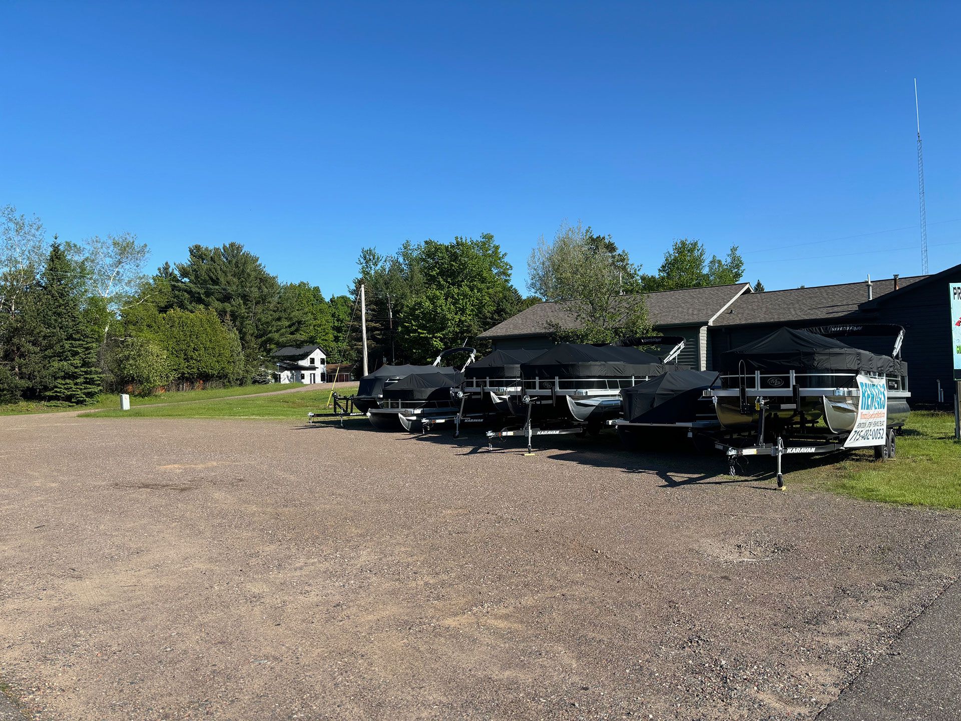 A row of boats are parked in a gravel lot in front of a house