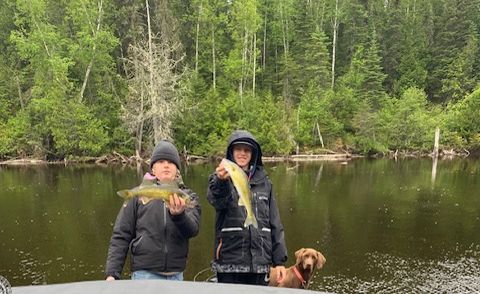 Two people and a dog are standing on a boat holding a fish