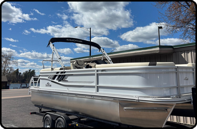 White pontoon boat on trailer parked outdoors under a blue sky with clouds